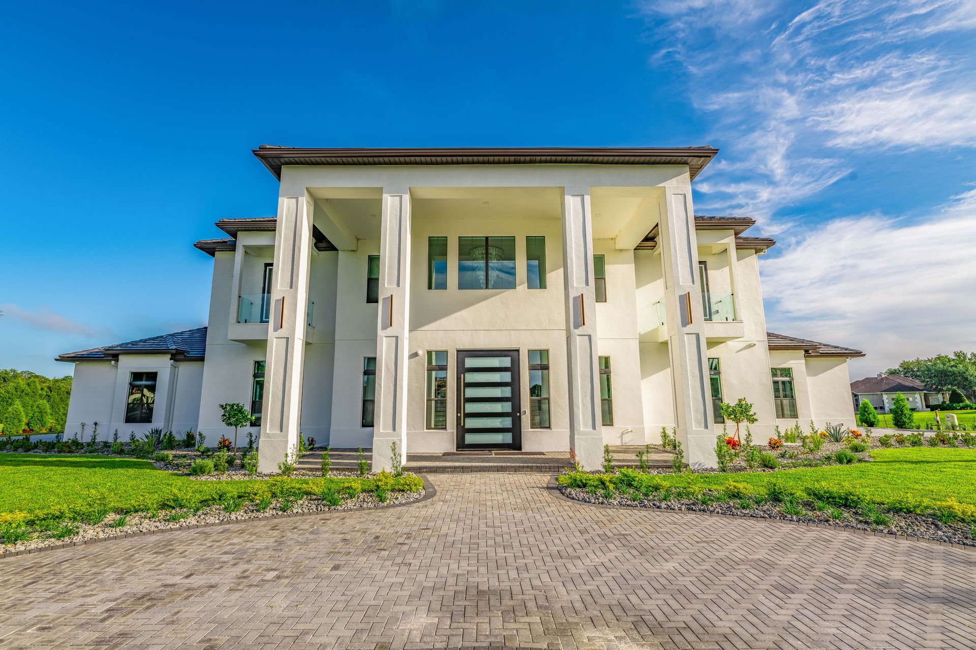 White mansion with columns, glass front door, and brick driveway under a blue sky.