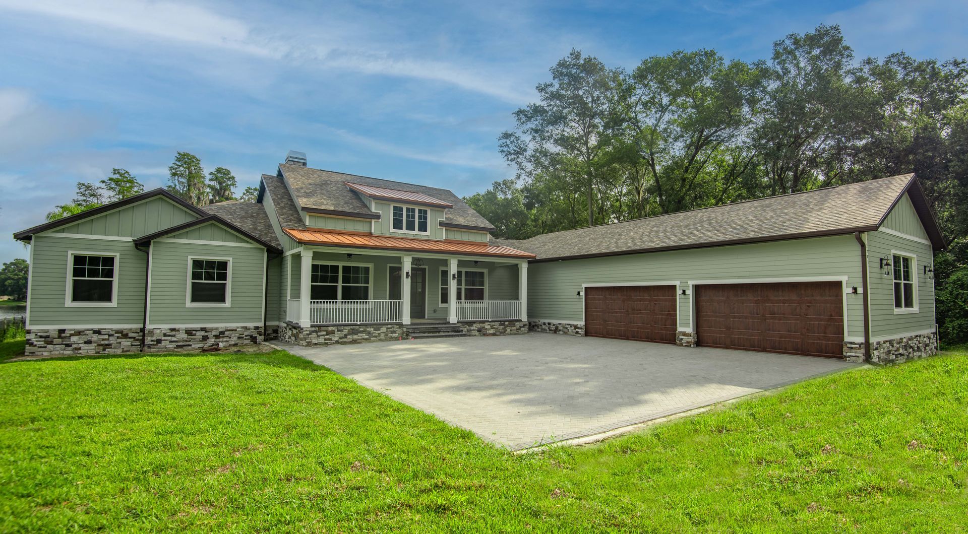 Green house with gravel driveway, attached garage, and lush green lawn under a blue sky.