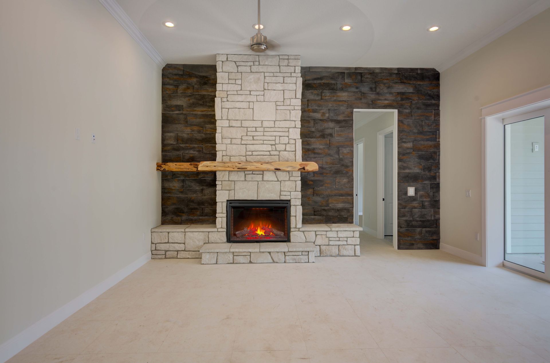 Empty living room with stone fireplace, brown accent wall, and ceiling fan. White walls, carpet, and trim.