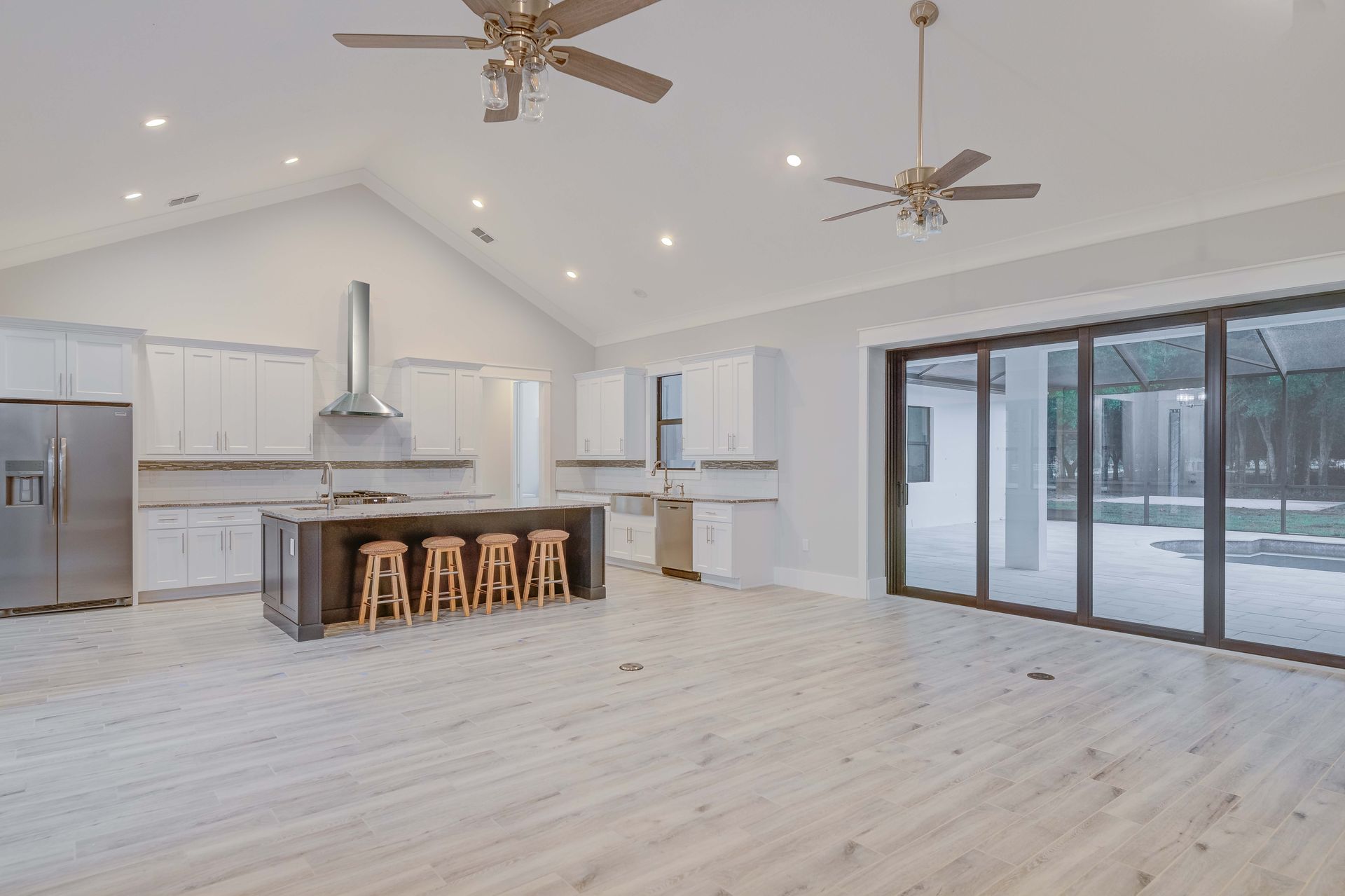 Bright, open kitchen with white cabinets, dark island with stools, stainless appliances, and large sliding doors.