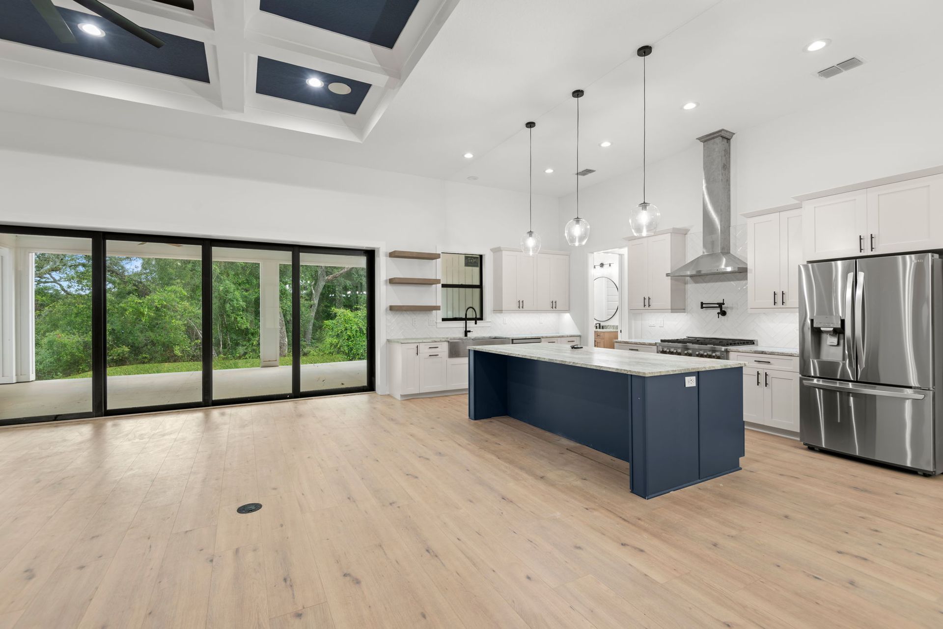 Modern kitchen with blue island, white cabinets, stainless steel appliances, and large sliding glass doors.