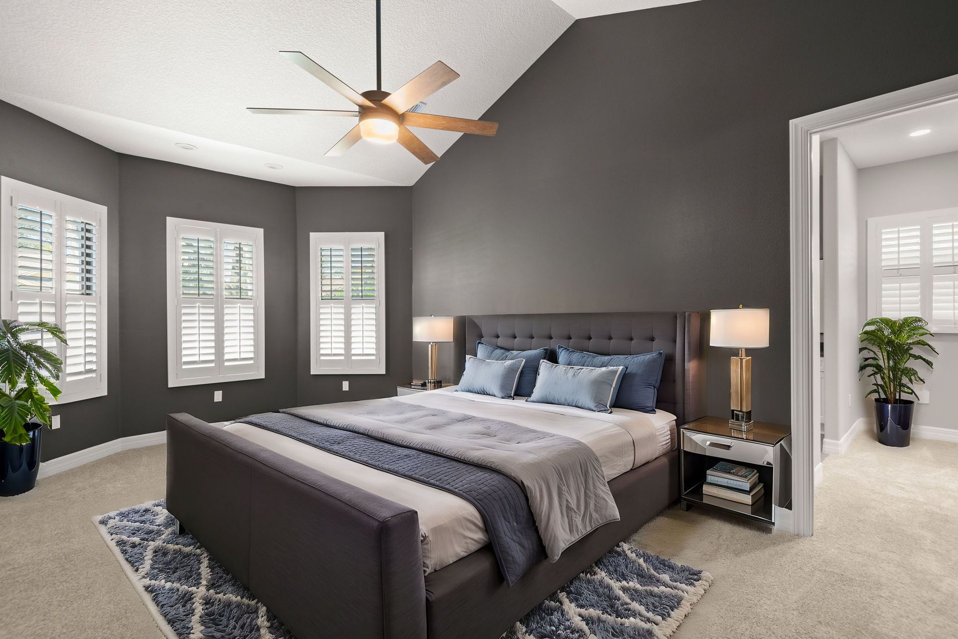 Bedroom with gray walls, bed, rug, shutters, and fan.
