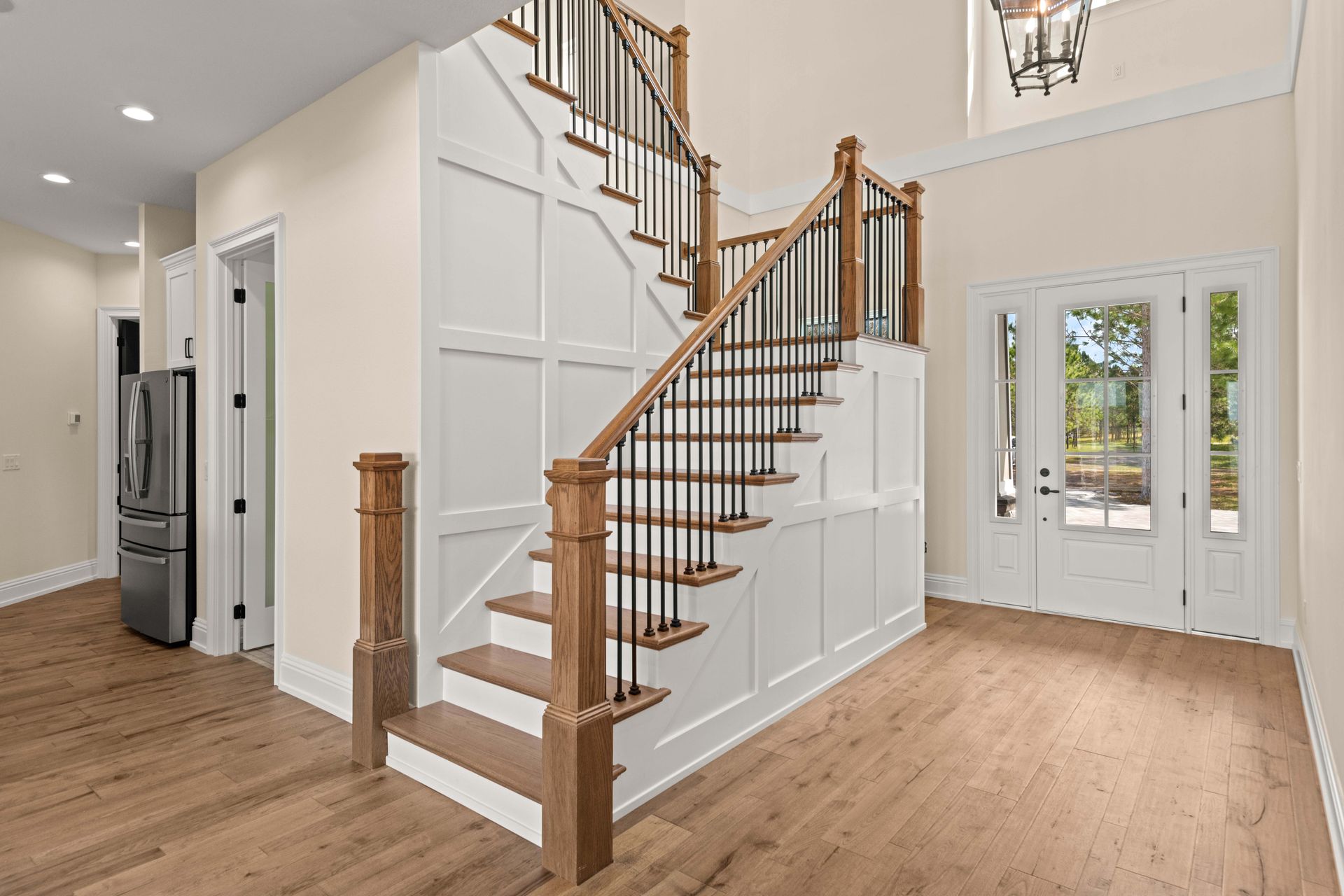 Wooden staircase in a home's entryway, with white paneling, and a door with glass panels.