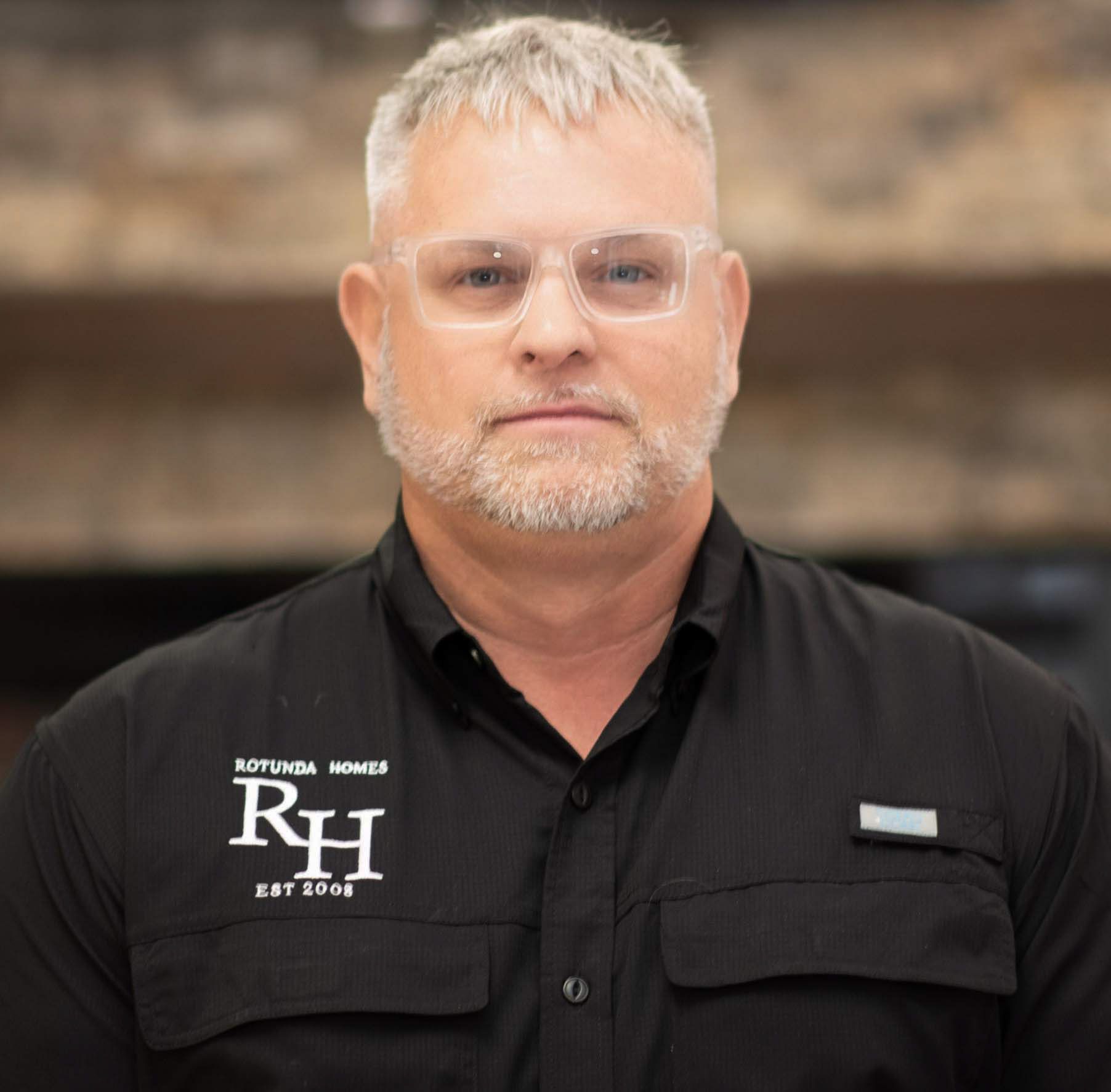 Man wearing glasses and a black shirt with logo.