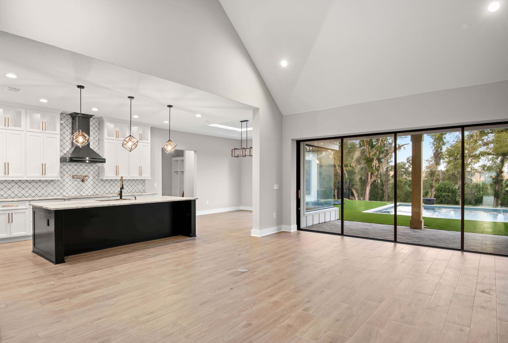 Open-concept kitchen and living area with black island, white cabinets, and large glass doors leading to a pool.