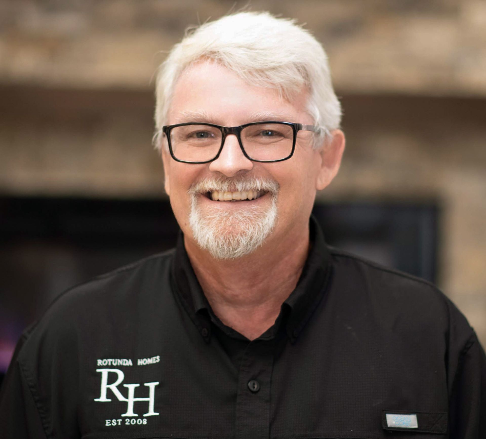 Man with glasses smiles, wearing black shirt with