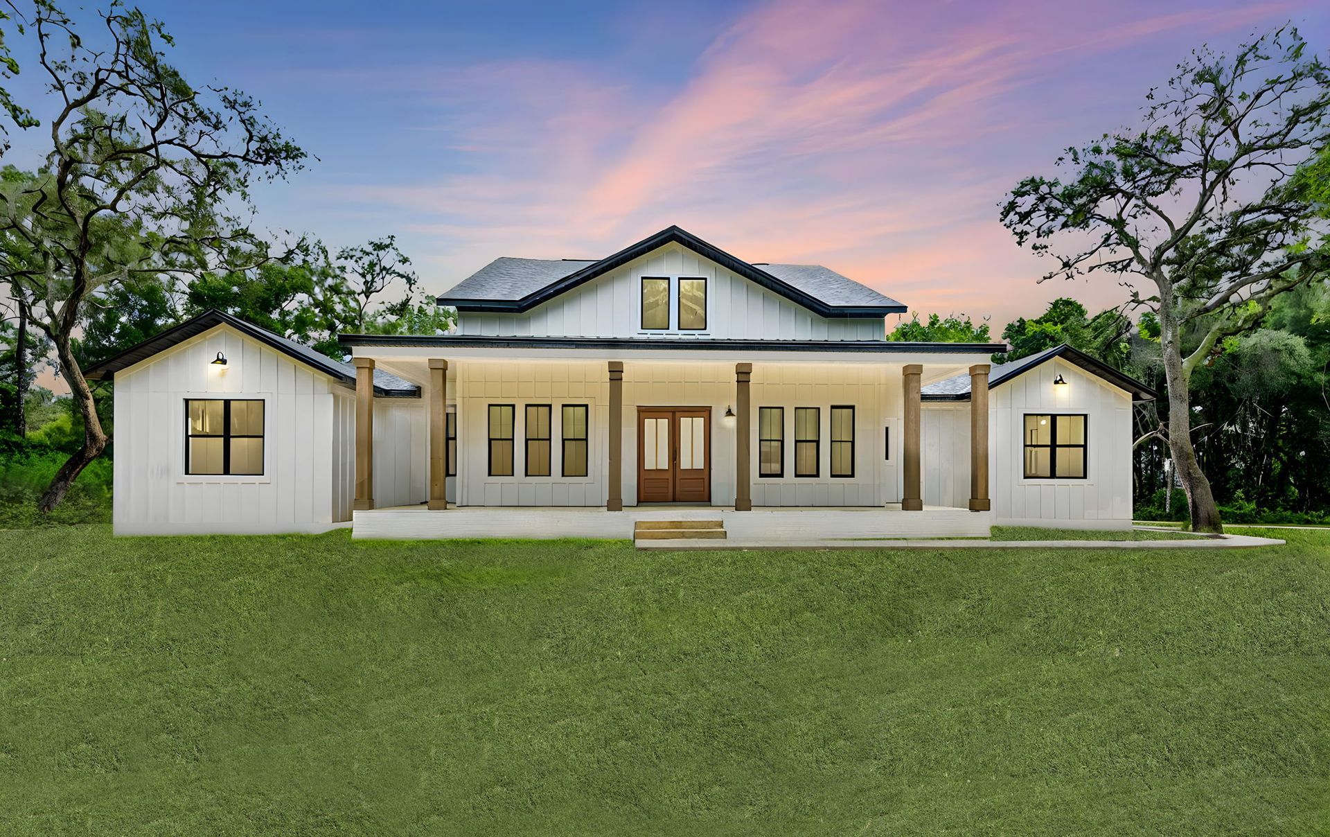White farmhouse with dark trim, porch, and two side structures against a sunset sky.