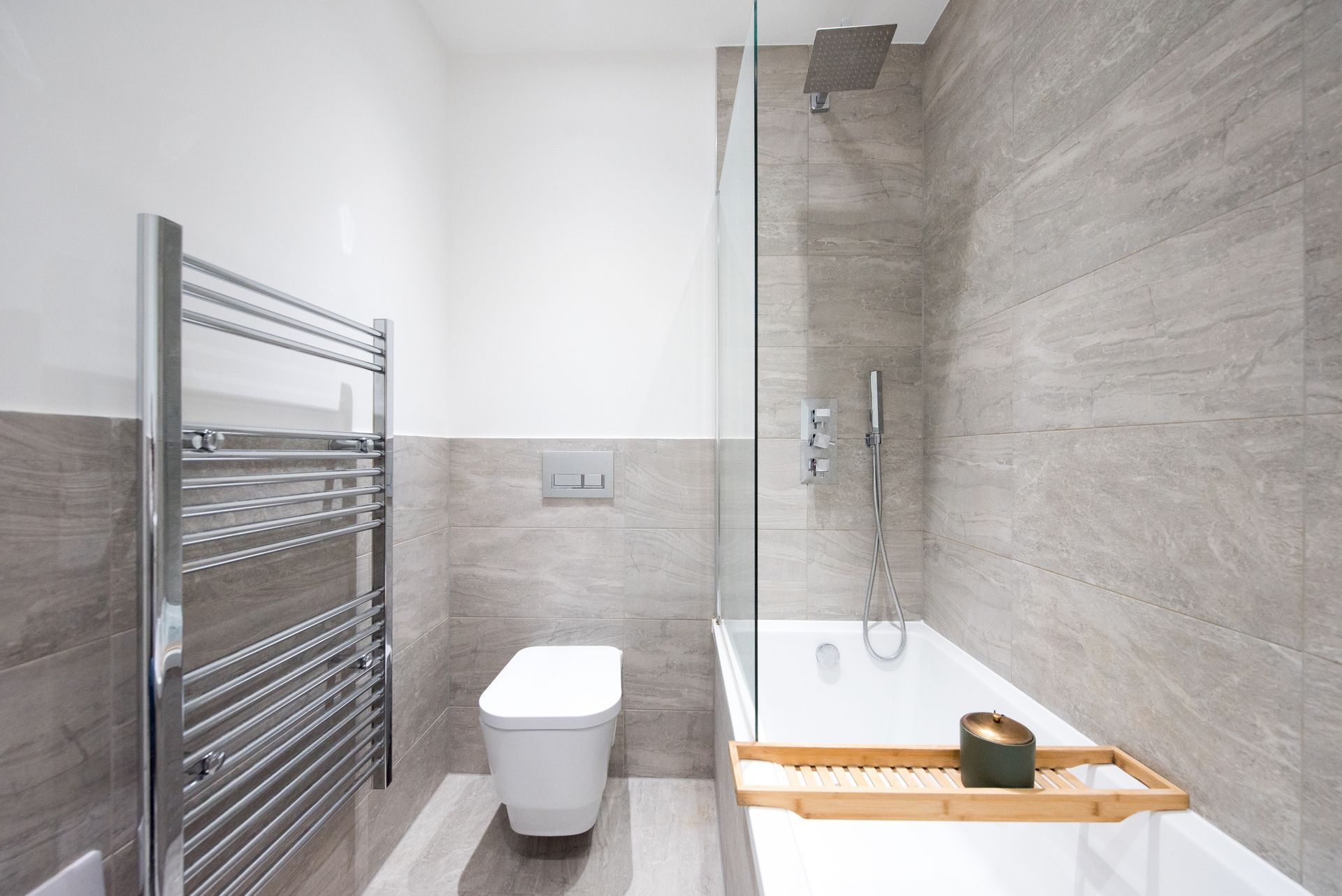 Bagno moderno con piastrelle grigie, WC, vasca da bagno, doccia e portasciugamani.