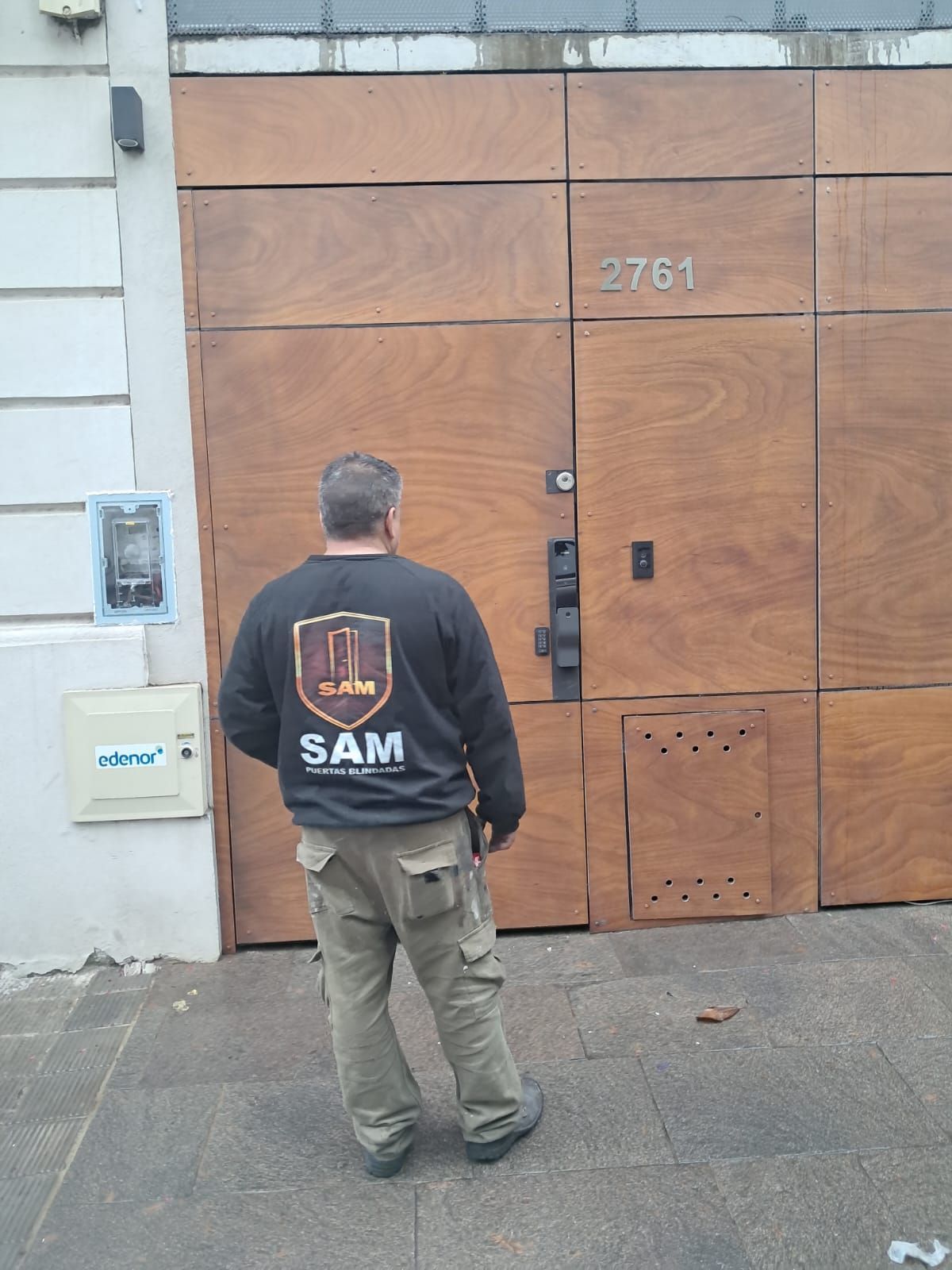 Una persona permanece de pie frente a una gran puerta de madera con el número 2781, vistiendo una chaqueta SAM.