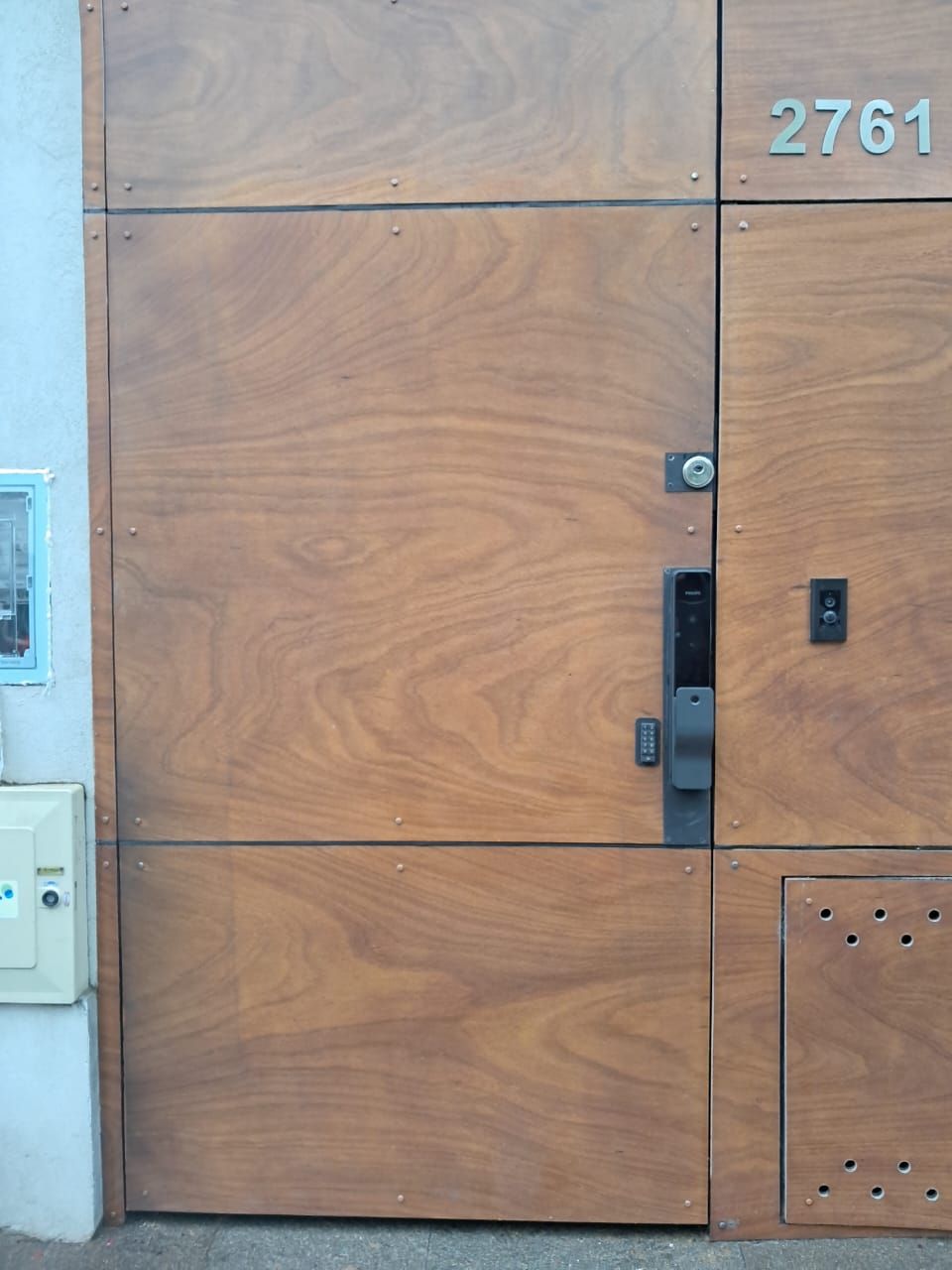 Puerta de entrada de madera con panel de acceso y número de dirección 2761.