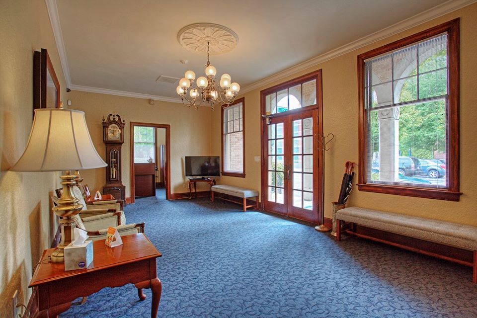 A living room with a clock , a table , a lamp and a bench.