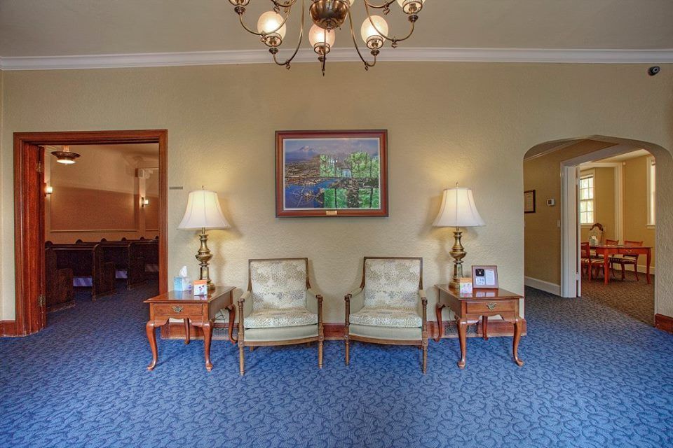 A living room with chairs , tables , lamps and a picture on the wall.