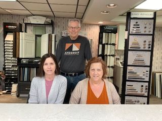 Three people standing in a kitchen showroom. Two women seated, one man standing behind them. They are smiling.