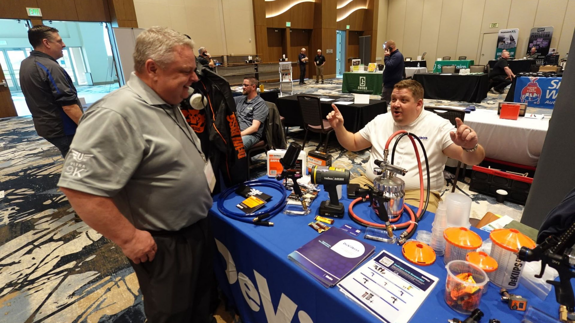 People at a booth discussing colorful robot parts and models on a blue table at an indoor expo