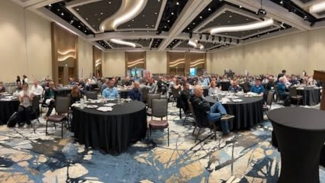 Banquet hall with seated attendees at round tables under modern curved ceiling lights