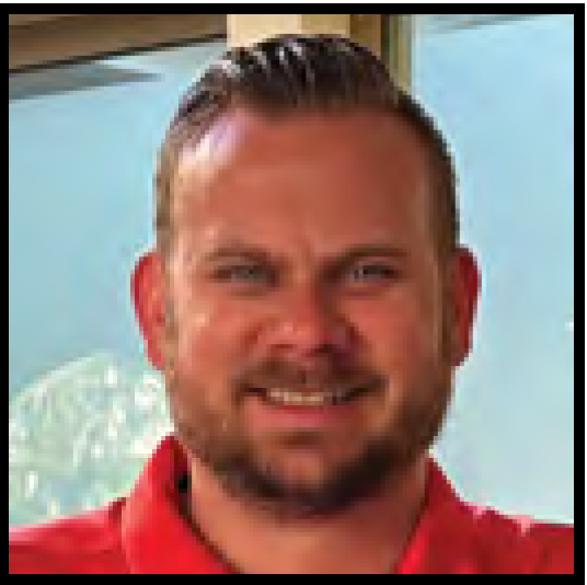 Smiling man in a red polo shirt indoors near a window with mountains in the background
