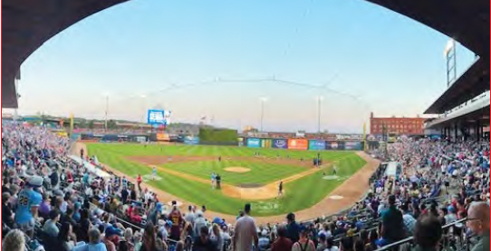 Baseball stadium with a crowd watching a game at sunset, viewed from behind home plate