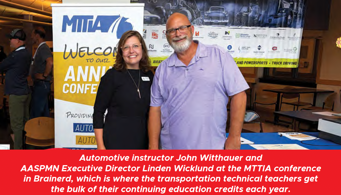 Two people smiling beside a MITA conference banner in an indoor event space.