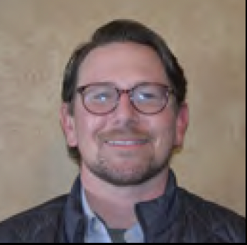 Smiling man wearing glasses and a dark jacket against a beige background