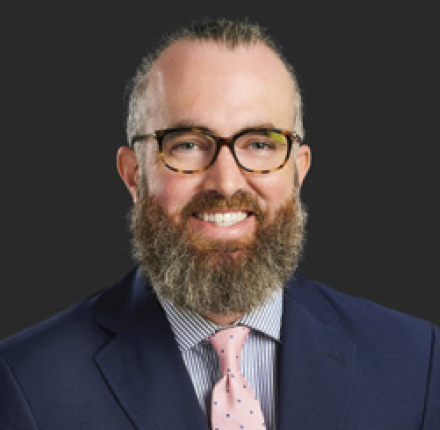 Smiling man in glasses and suit with pink tie on dark background
