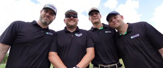 Four men in black shirts and caps smiling, standing close together outdoors.