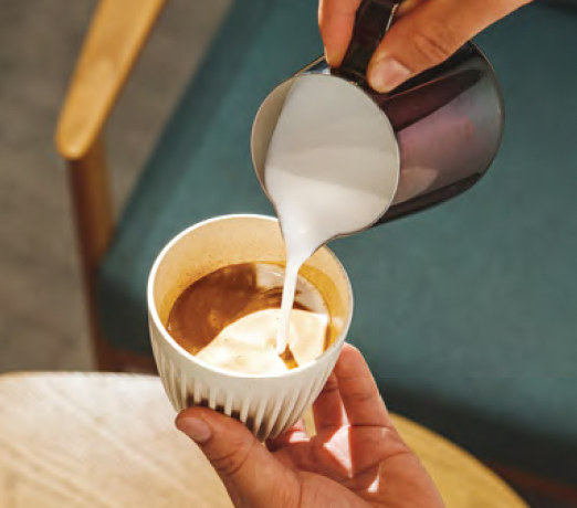 Milk being poured into a cup of coffee held in a hand