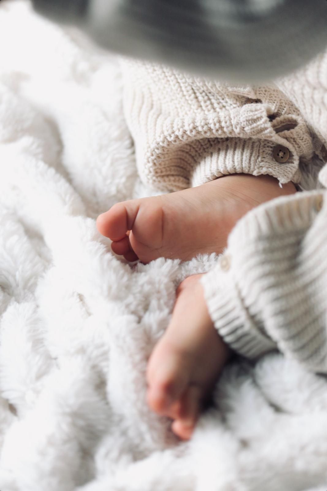 Een slapende baby in een crèmekleurig gebreid truitje ligt op een zachte witte deken.