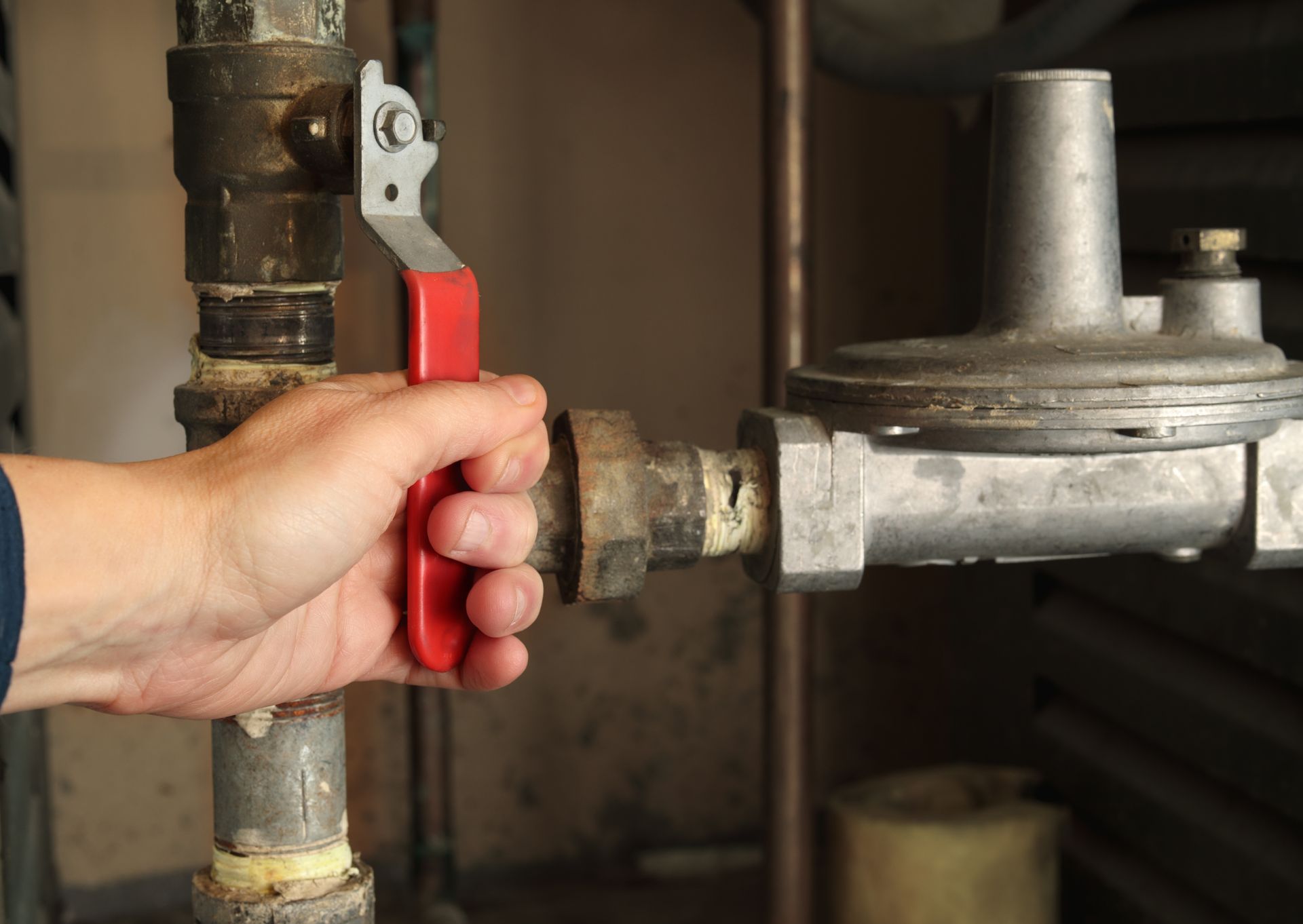 Hand turning a red lever valve on a metal pipe in a basement or utility room