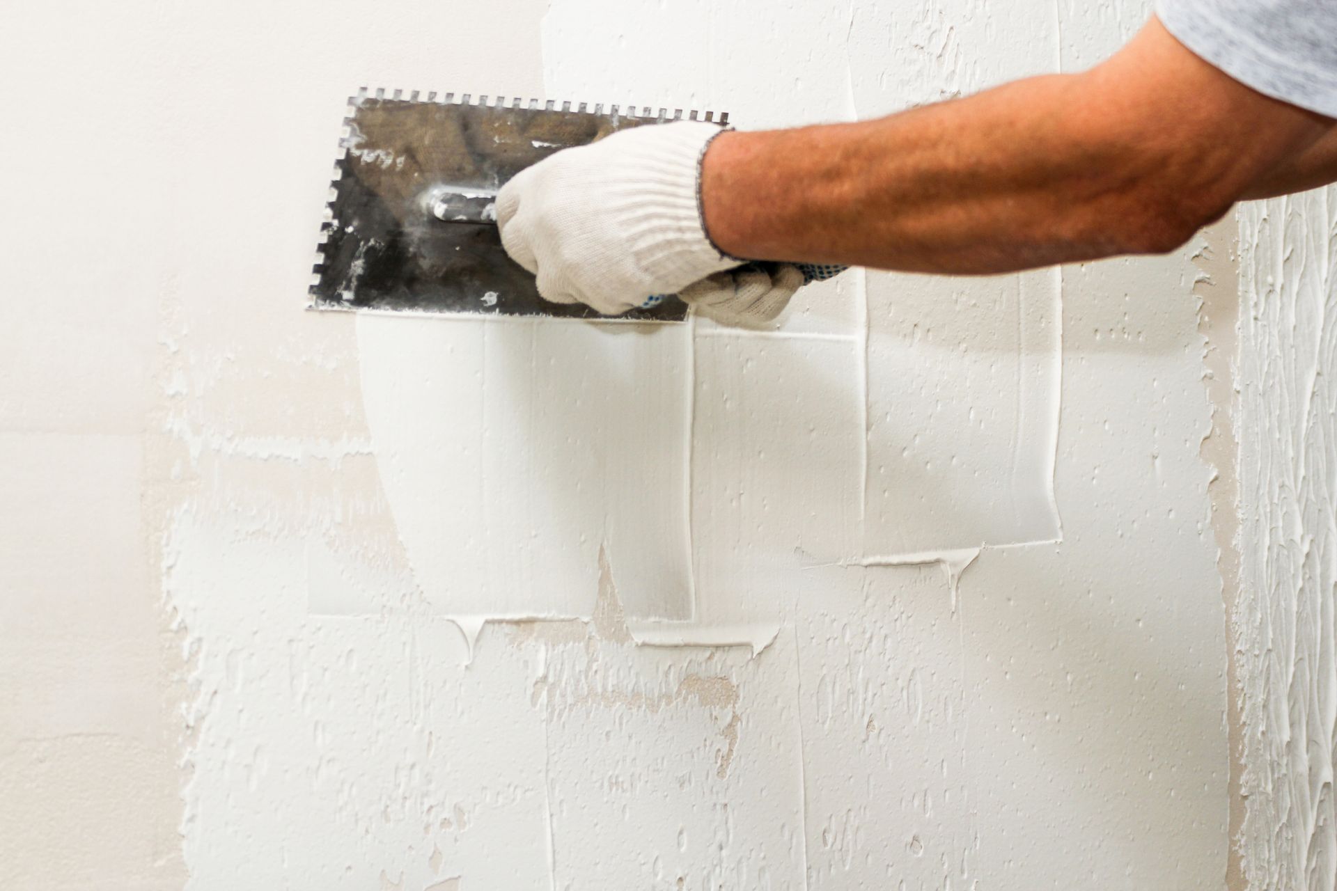 Two construction workers inside a building, one on the floor, one at a wall, working.