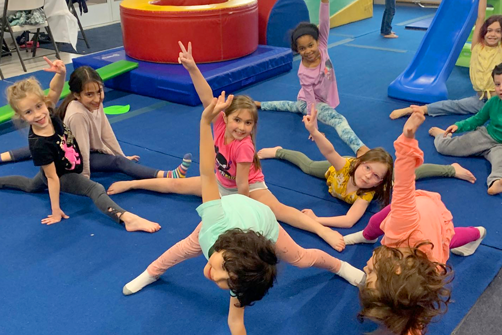 A group of young girls are doing splits on a gym floor.