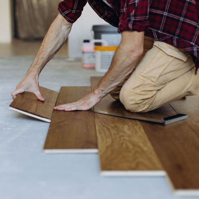 Person installing brown wood flooring planks on a floor indoors
