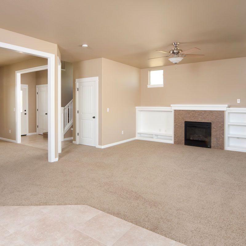 Empty beige living room with carpet, fireplace, ceiling fan, and open doorway to hall