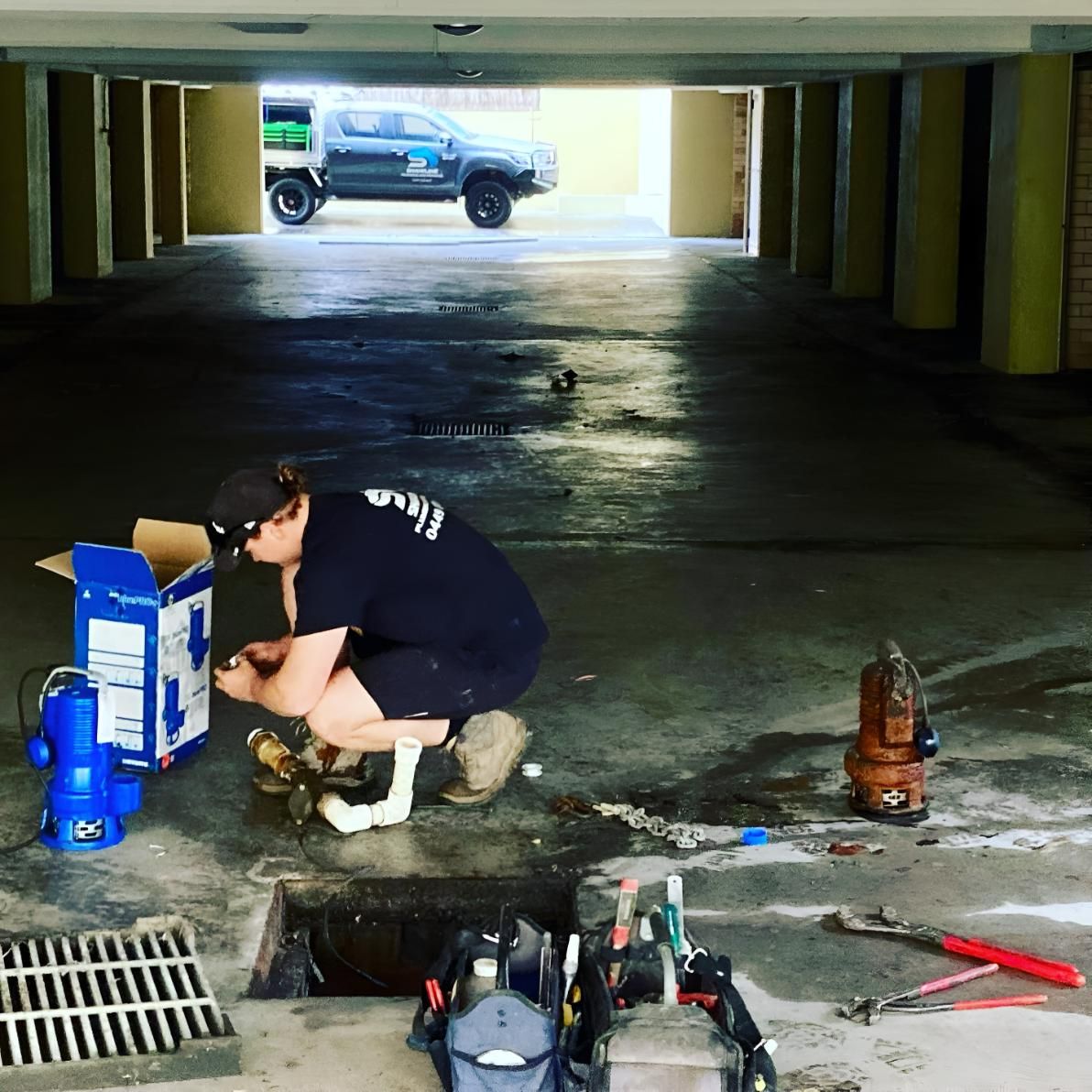 A Man is Working on a Drain in a Garage — Shawline Plumbing and Drainage In Iluka, NSW