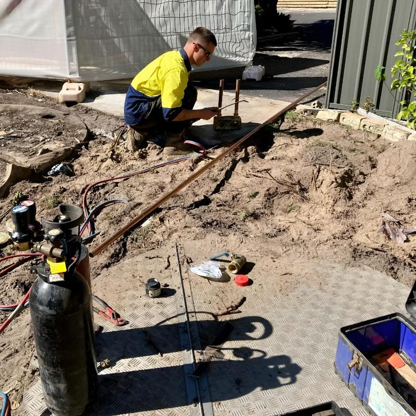 A Man is Kneeling Down in the Dirt Working on a Piece of Metal — Shawline Plumbing and Drainage In Iluka, NSW