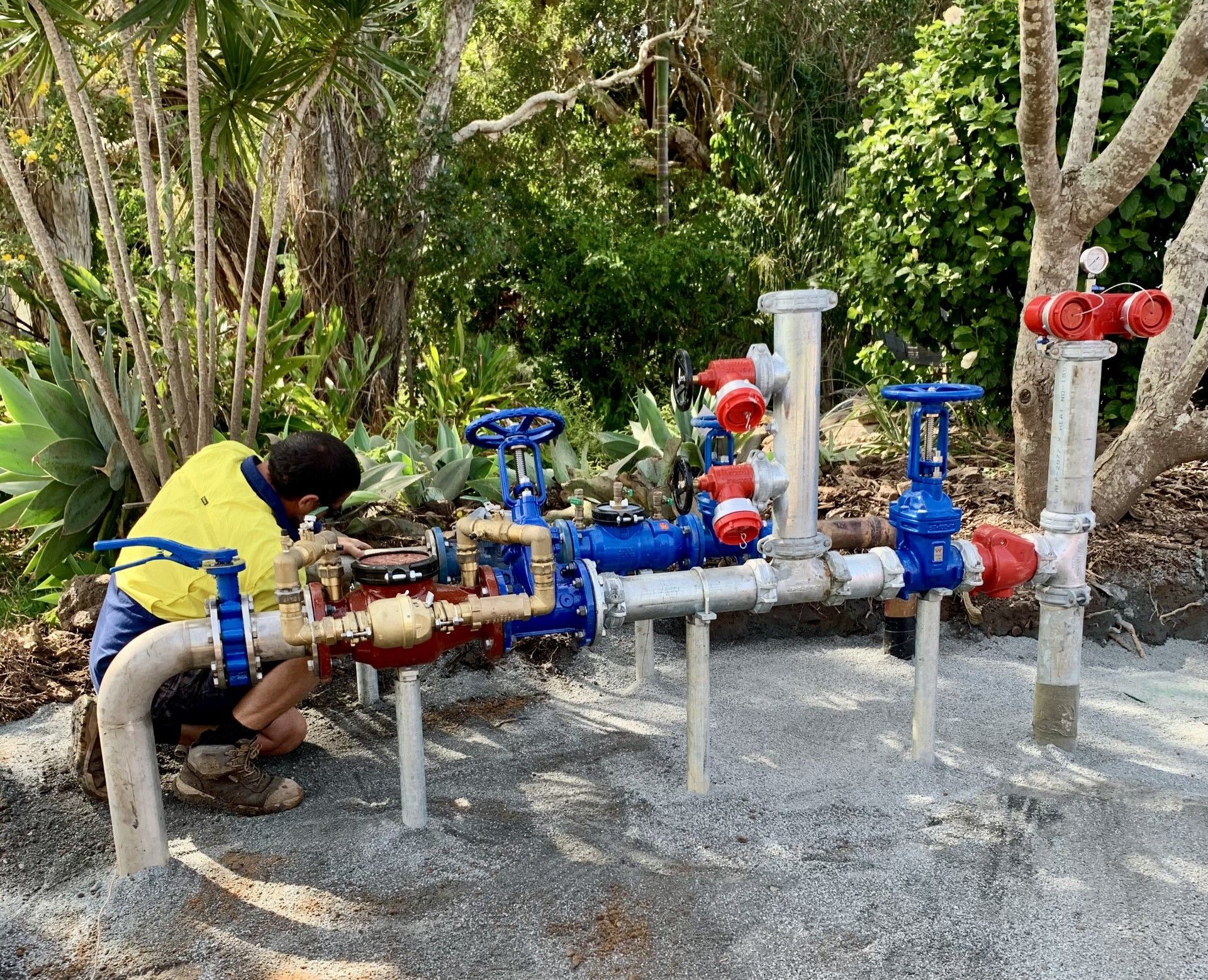 A Man is working on a set of pipes outside in front of a garden— Shawline Plumbing and Drainage In Iluka, NSW