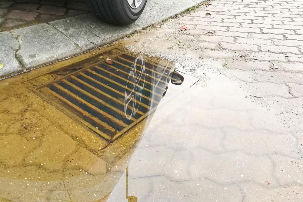Puddle Reflecting a Bicycle, Next to a Street Drain and a Car Tire on a Brick Sidewalk — Shawline Plumbing and Drainage In Iluka, NSW