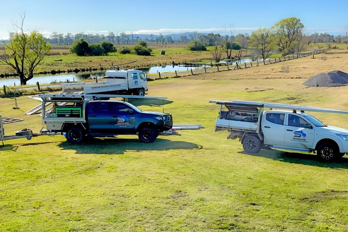 Two Trucks Are Parked in a Grassy Field Next to a River — Shawline Plumbing and Drainage In Iluka, NSW