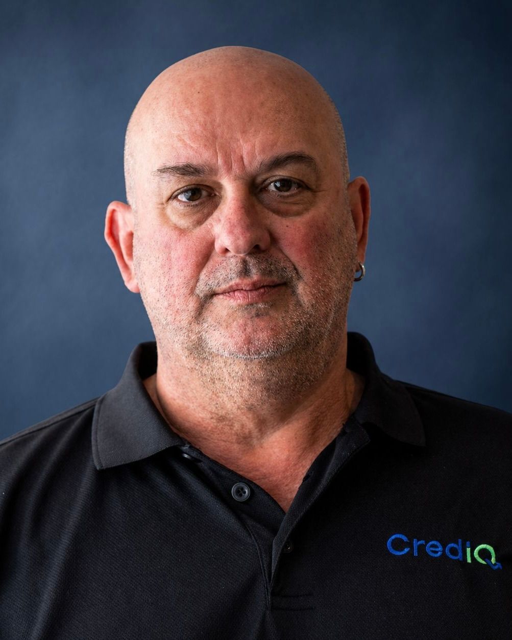 Clive Fletcher wearing a grey polo shirt with a Crediq logo against a plain, textured off-white wall.