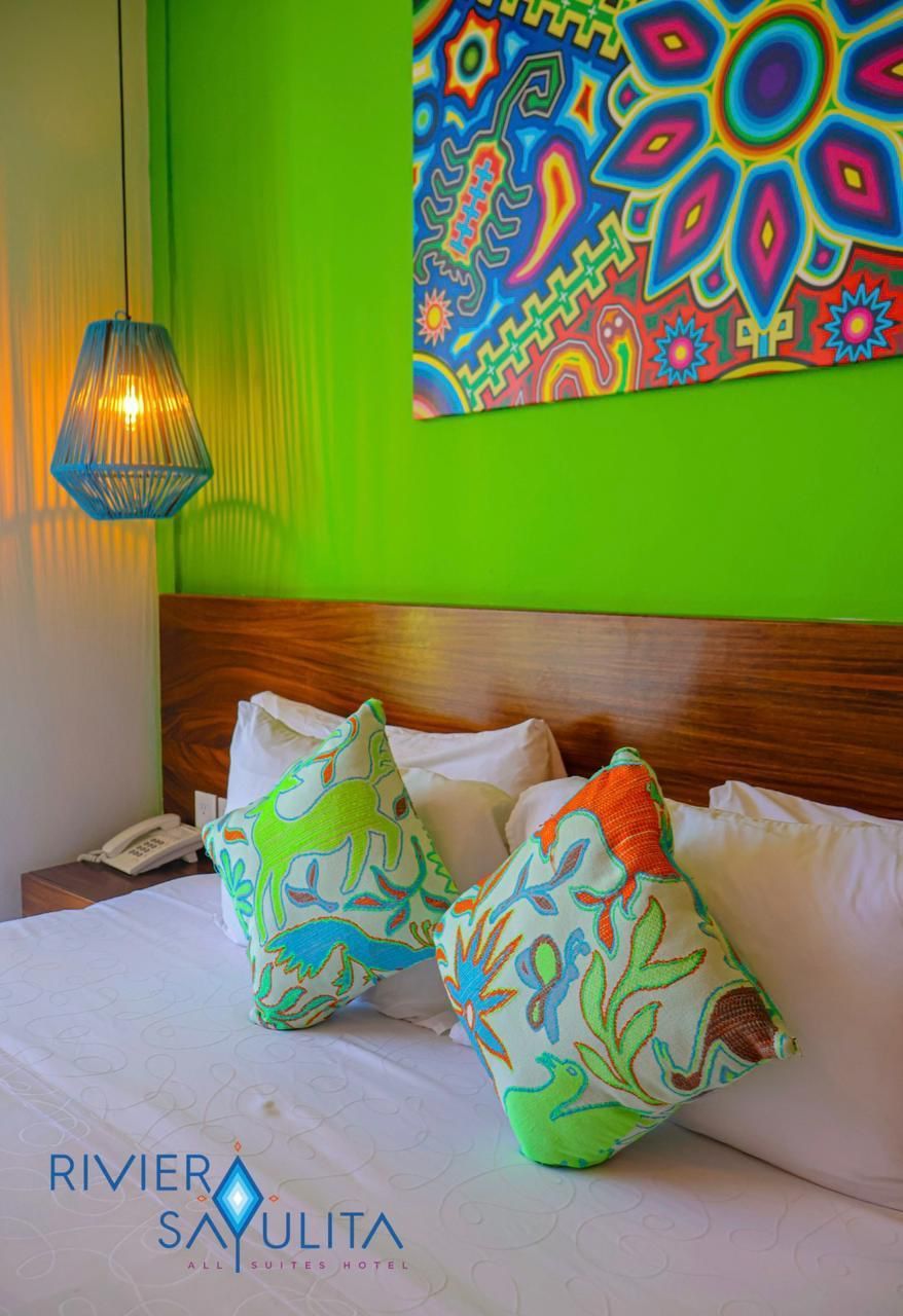 A bed with colorful pillows and a painting on the wall.