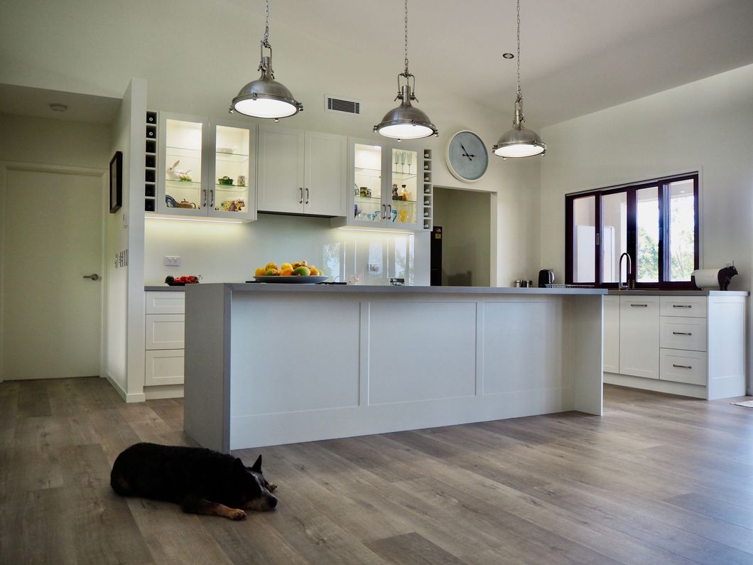 Modern kitchen with a large island, pendant lights, and a dog lying on the wood floor.