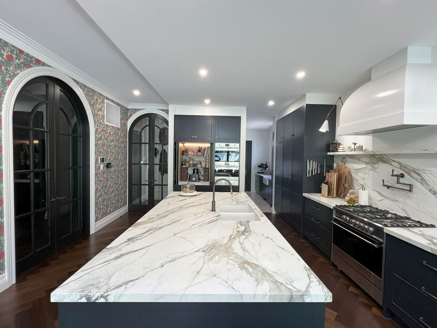 Modern kitchen with marble island, dark cabinets, stainless steel appliances, and floral wallpaper.