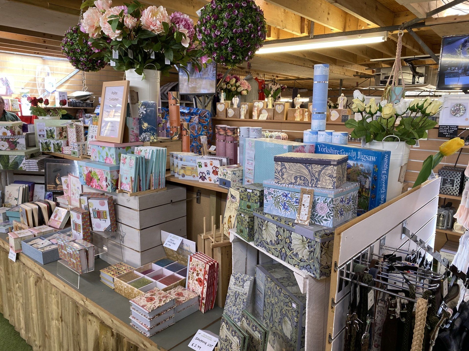 A display of cards, boxes, and gifts in a shop. Flowers and hanging decor overhead.
