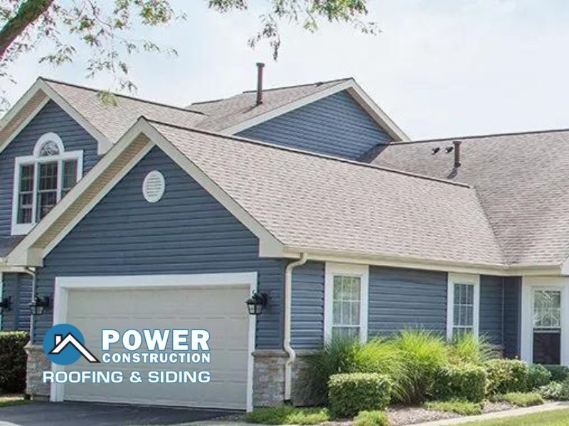 A blue house with a gray roof is being built by power construction roofing and siding.