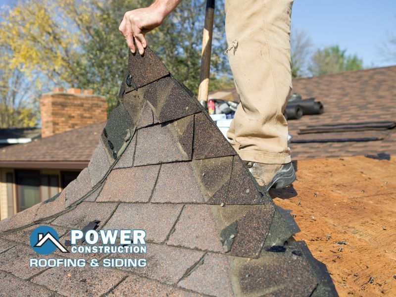 A man is working on a roof with power construction roofing and siding written on the bottom