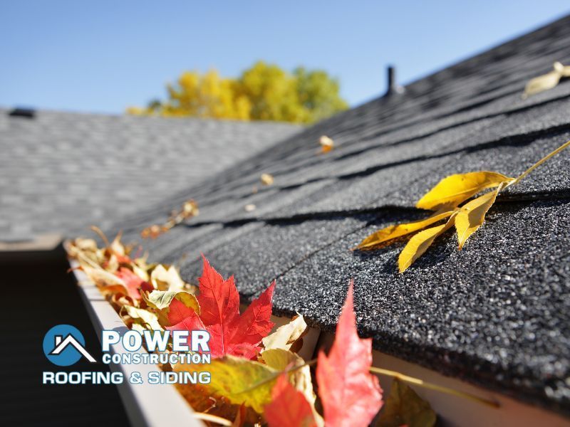A gutter full of leaves on a roof with a power construction logo in the corner