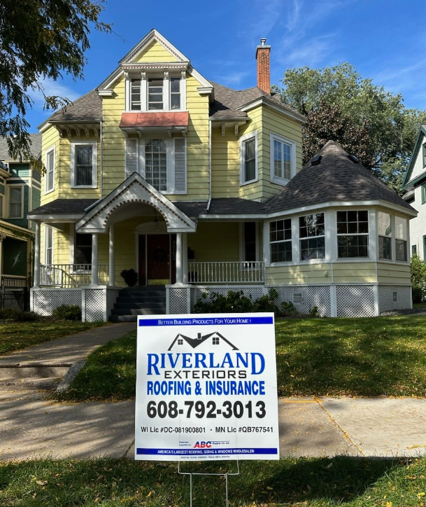 Yellow Victorian house with Riverland Exteriors sign on lawn.
