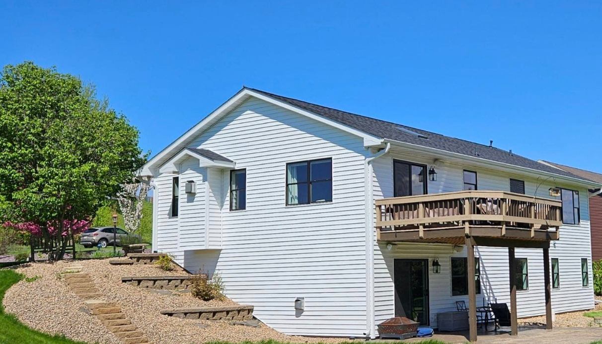 White house with a wooden deck, black windows, and a blue sky in the background.