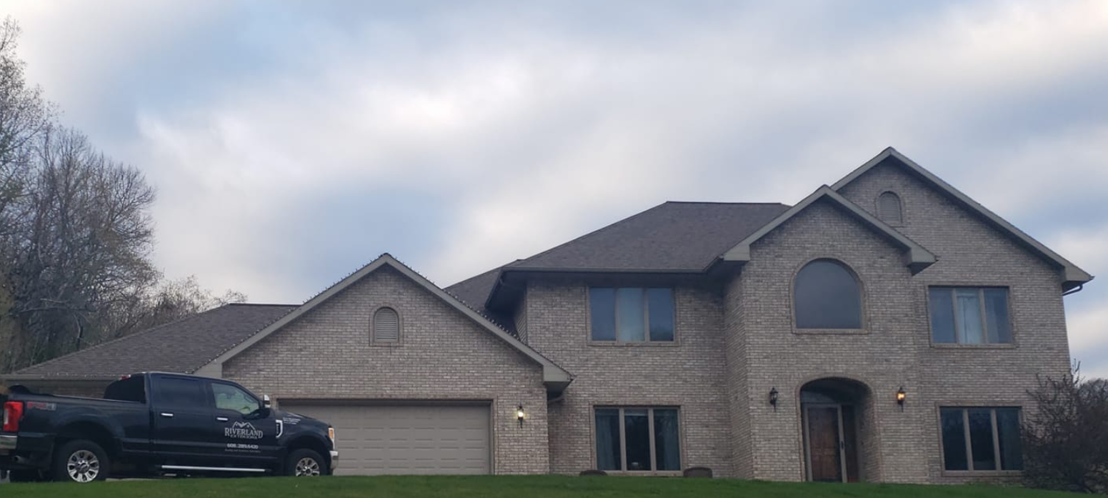 A two-story brick house with a dark pickup truck parked in front. Cloudy sky in the background.