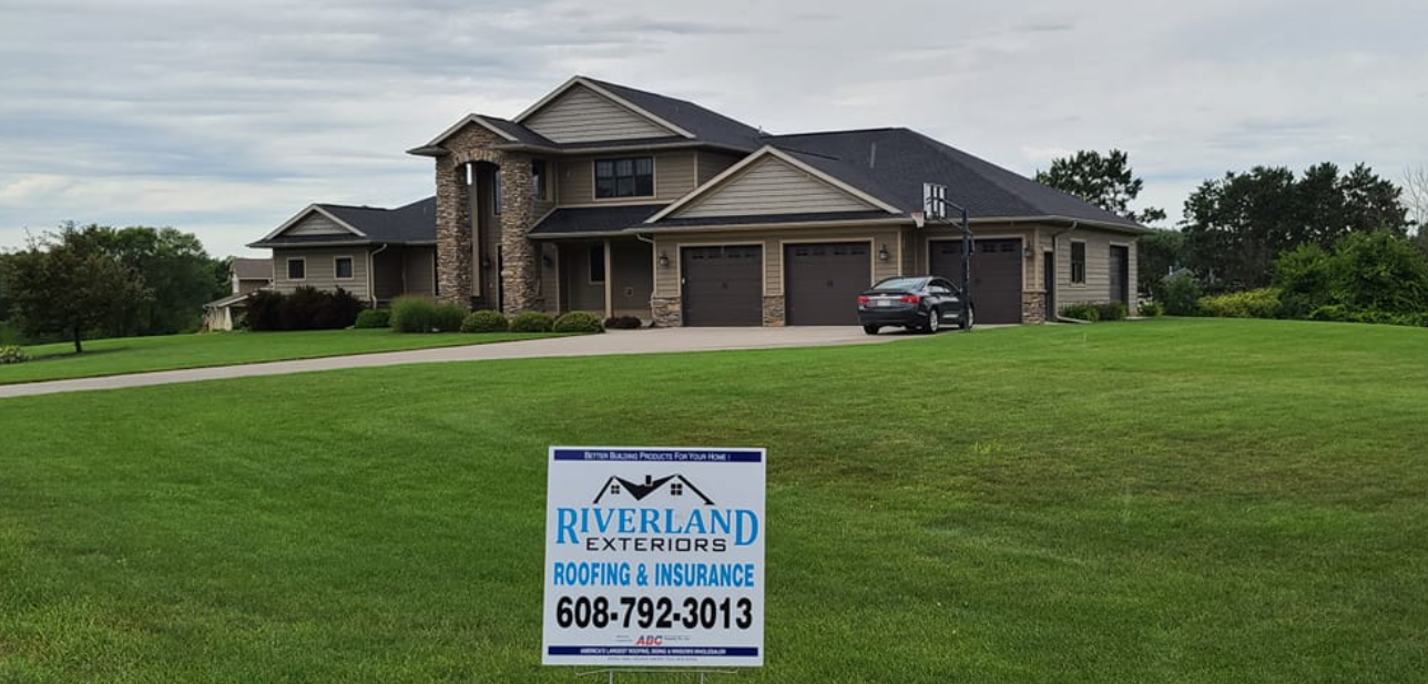 Large house with garage, sign in front, cloudy sky.