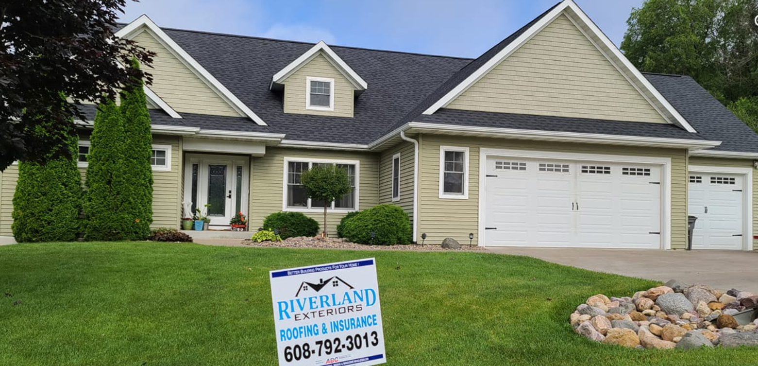 A house with a green lawn and a sign for Riverland Roofing.